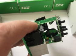 Zbliżenie na dłoń trzymającą układ elektroniczny z zieloną płytką PCB i elementami elektronicznymi.