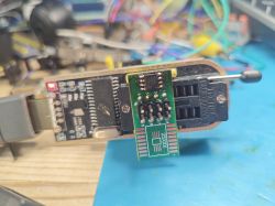 USB programmer with SOIC8 adapter for 25XXX EEPROM on a workbench.