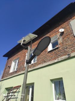 Lampa solarna zamontowana na słupie przed ceglaną ścianą budynku.