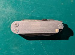Zamknięty scyzoryk z aluminiową okładziną i czterema śrubami na zielonej macie