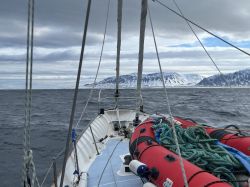 Yacht on Arctic Waters with View of Snow-Covered Mountains View from the yacht on calm ocean waters and snow-covered mountain shores in the distance.