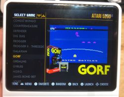 White retro handheld console displaying Atari 5200 game selection menu with preview of Gorf