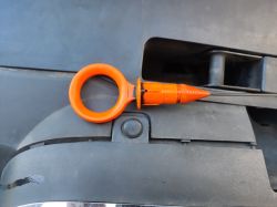 Pomarańczowy bagnet silnika bez uszczelki, leżący na czarnym plastiku pod maską