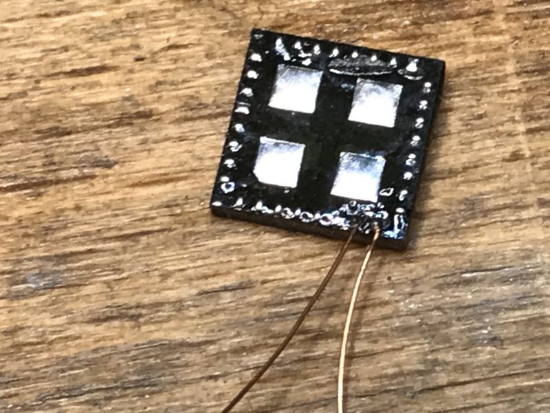 Integrated Circuit on Wooden Surface Small electronic chip with four metallic squares on a brown background.