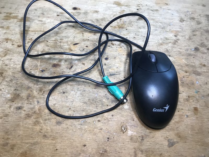 Old Genius Computer Mouse with PS/2 Plug Old Genius computer mouse with cord and PS/2 plug on a wooden surface.
