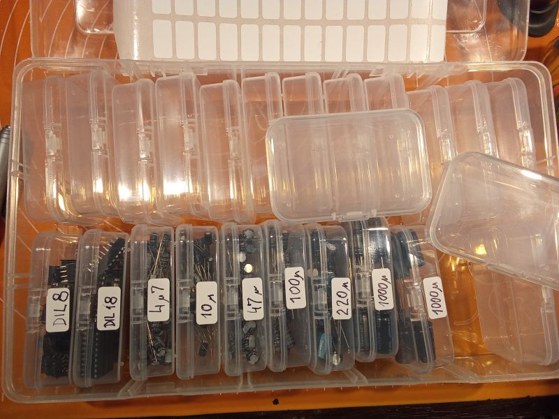 Pudełko z małymi plastikowymi pojemnikami na elementy elektroniczne, oznaczone etykietami z wartościami.
