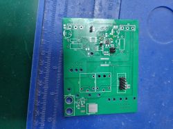 Zielona płytka PCB z kilkoma wlutowanymi komponentami, leżąca na niebieskiej macie z linijką.