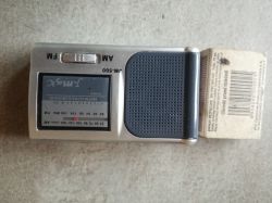 A small silver Jmax JM-500 portable radio is placed next to a box of matches on a light surface.