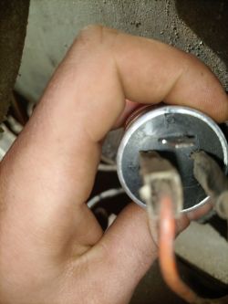 Osoba trzyma metalowy element z trzema wypustkami, z podłączonymi kablami czerwonym i czarnym.