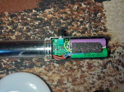 Wnętrze lampki LED z widoczną elektroniką i akumulatorami na dywanie.