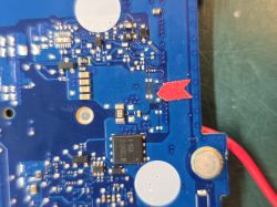 Fragment niebieskiej płytki PCB z układami SMD i czerwonym znacznikiem wskazującym pole lutownicze
