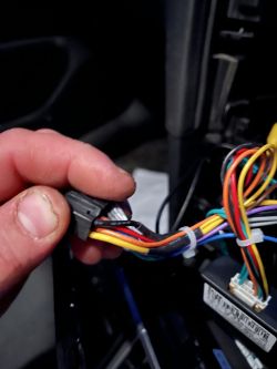 Osoba trzyma wiązkę przewodów samochodowych z kostką.