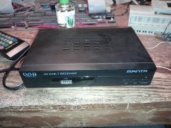 Tuner DVB-T Manta z pilotem na drewnianym stole.