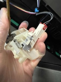 Ręka trzyma plastikowy mechanizm z wystającym czarnym trzpieniem i podłączonymi przewodami
