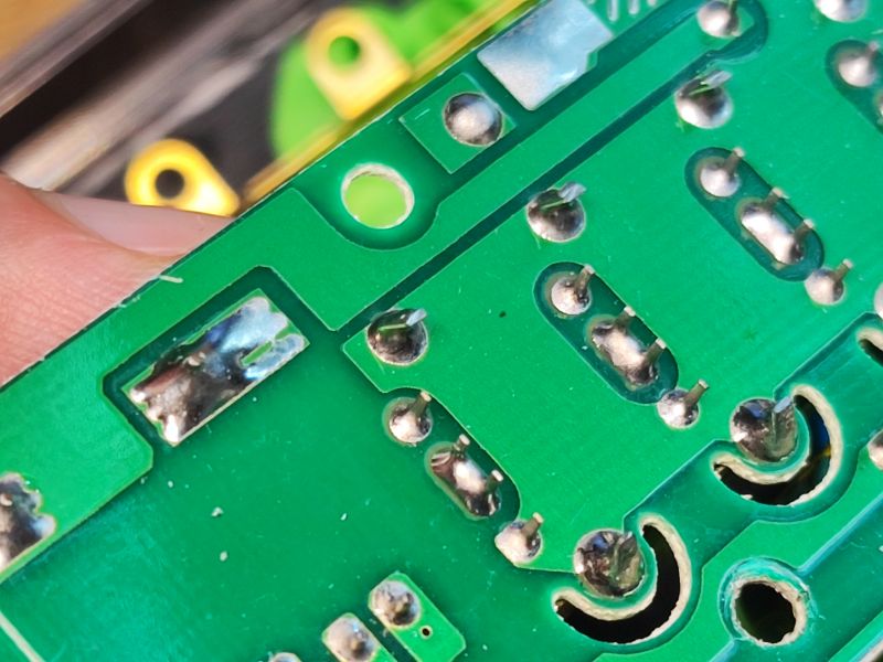 Zbliżenie na płytkę drukowaną z widocznymi lutami oraz zieloną powierzchnią PCB, niektóre połączenia wyglądają na niestarannie wykonane.