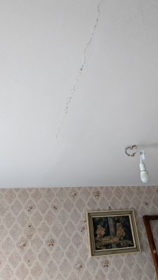 Pęknięcie na suficie z wiszącą żarówką i obrazem na ścianie.