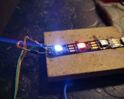 Flashing WS2812B LED strip connected with wires to a breadboard on a white surface.