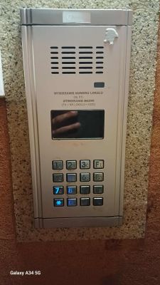 Panel domofonowy Genway z klawiaturą numeryczną i kratką głośnika na ścianie.