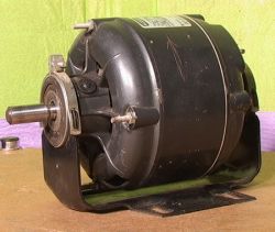 Stary silnik elektryczny o cylindrycznym kształcie na tle kolorowej ściany.