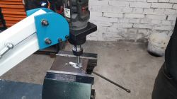Gewindearm mit Bohrhalter Gewindearm mit einer am Metallhalter befestigten Bohrmaschine, die an einem Metallstück arbeitet.