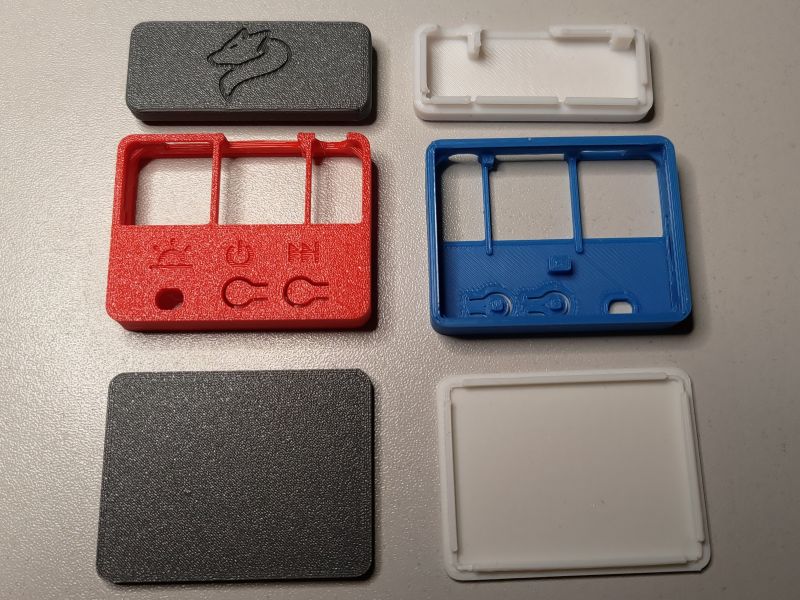 Four 3D-printed enclosure parts in different colors laid out on a desk