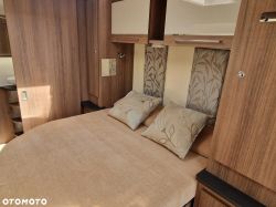 Interior of a camper with a comfortable bed and wooden cabinets.