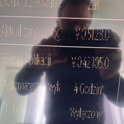 Informacje o wersjach oprogramowania na ekranie TV Ekran informacji TV z wersją oprogramowania V.051.80 i aplikacji V.042.195.0, widoczne odbicie osoby