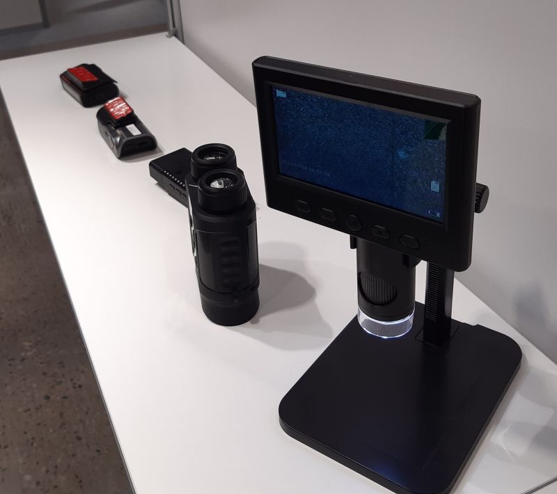 Mikroskop cyfrowy z wyświetlaczem i luneta na białej powierzchni stoisku targowym.