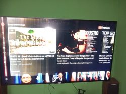 Telewizor wyświetla ekran z rekomendacjami YouTube, w tym filmy o muzyce bossa nova i akustycznych coverach.