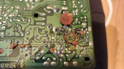 Spód zielonej płytki PCB z lutami i dołączonymi kondensatorami, w tym dyskowym „413 KCK”.