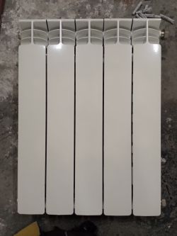 Grzejnik aluminiowy z 5 pionowymi żeberkami ustawiony na betonowej podłodze