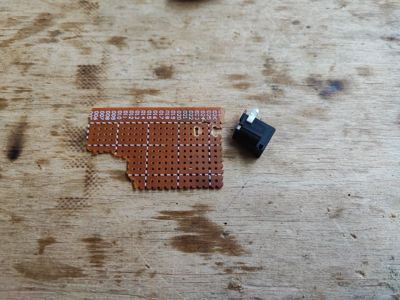 Prototype Board and DC Jack Connector Perforated prototype board and DC jack connector on a wooden table.