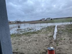 Podwórko po deszczu z wodą zalewającą teren w pobliżu ogrodzenia.