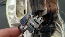 Zbliżenie na metalową kostkę elektryczną z podłączonymi przewodami brązowym, niebieskim i białym w urządzeniu elektrycznym.