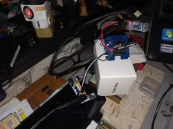 Electronic boards connected with wires on a cluttered desk with tools, glasses, and paper notes.