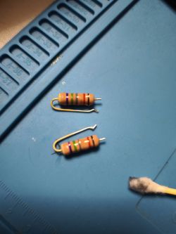 Dwa rezystory osiowe z kolorowymi paskami leżą na niebieskiej macie serwisowej