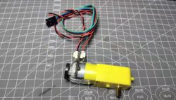 Electric Motor with Encoder on Measuring Mat A yellow electric motor with an encoder and wires lies on a measuring mat.