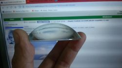 Dłoń trzyma półkulistą soczewkę szklaną na tle ekranu z forum internetowym