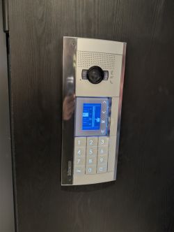 Panel wideodomofonu Bticino z kamerą, ekranem LCD i klawiaturą numeryczną na ciemnych drzwiach