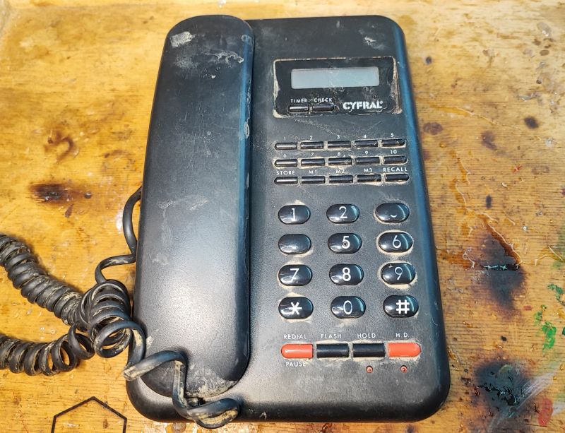 Stary telefon stacjonarny Cyfral C 928 T/P z wyświetlaczem i numerami na przyciskach, leżący na drewnianej powierzchni.