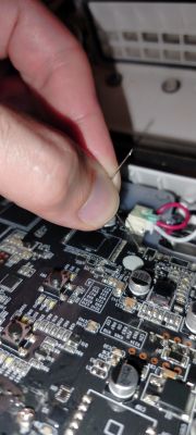 Finger holds a thin wire shorting pins on a black PCB with electronic components.