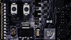 Zbliżenie płytki PCB z elementami SMD; widać odbicia światła na czarnym laminacie.