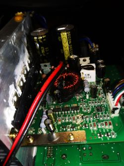 Wnętrze subwoofera Monacor Sound 100sub z widocznymi elementami elektronicznymi, w tym cewką i kondensatorami.