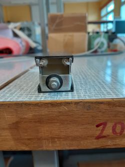 Metalowy element z dwiema śrubami i okrągłym trzpieniem na blacie stołu warsztatowego