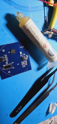 PCB with SMD components, BGA flux, and tweezers on a blue background.