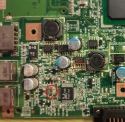 Zbliżenie na płytę główną z widocznymi kondensatorami i innymi elementami elektronicznymi, zaznaczonymi czerwonymi prostokątami i kołkiem.