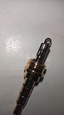 Metalowy łącznik z otworem na końcu leży na jasnym tle.