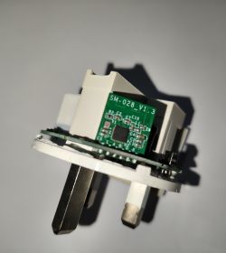 Inside a smart plug: PCB marked “SM-028_V1.3” in a white housing with metal prongs