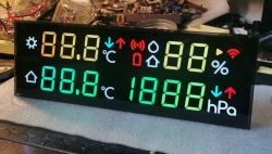 LED weather-station display with multicolor 7-segment digits and icons on a cluttered electronics workbench