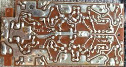 Spód brązowej płytki PCB z lutami i ścieżkami; widoczne napisy „2215-102” i „TORAL”.